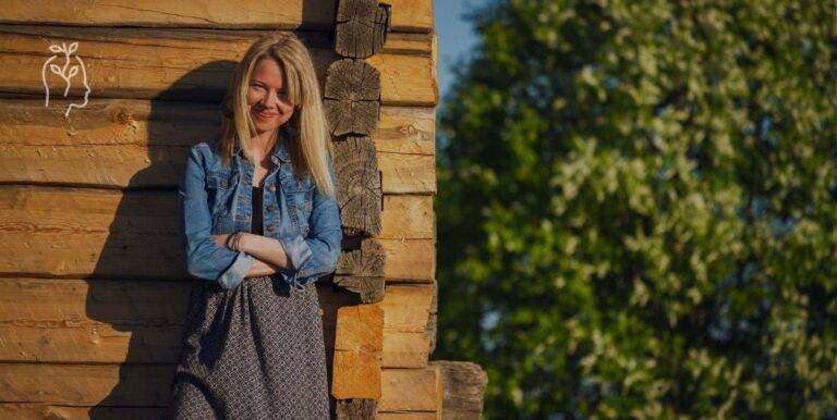Femme se tenant devant une maison en bois et qui sourit