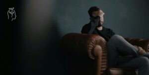 Homme anxieux assis sur un sofa qui se prend la tête dans ses mains
